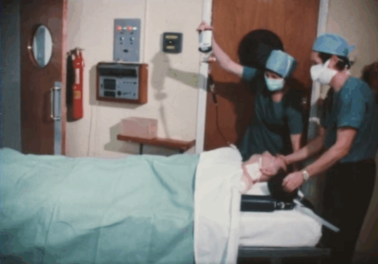 Two healthcare professionals administer a blood transfusion to a patient unconscious on a hospital bed. 